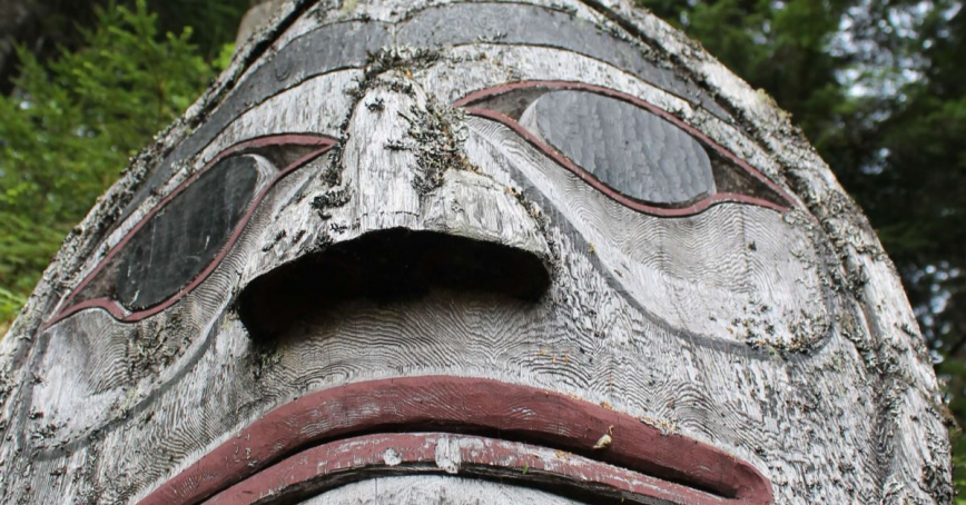 A tight image of a face on a weather-worn totem pole.